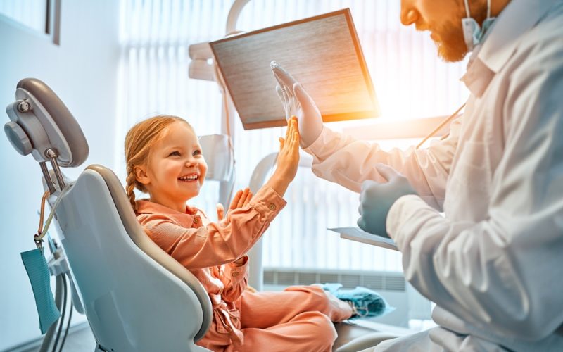 A,Little,Girl,Is,Sitting,In,A,Dentist’s,Chair,,Giving A,Little,Girl,Is,Sitting,In,A,Dentist's,Chair,,Giving